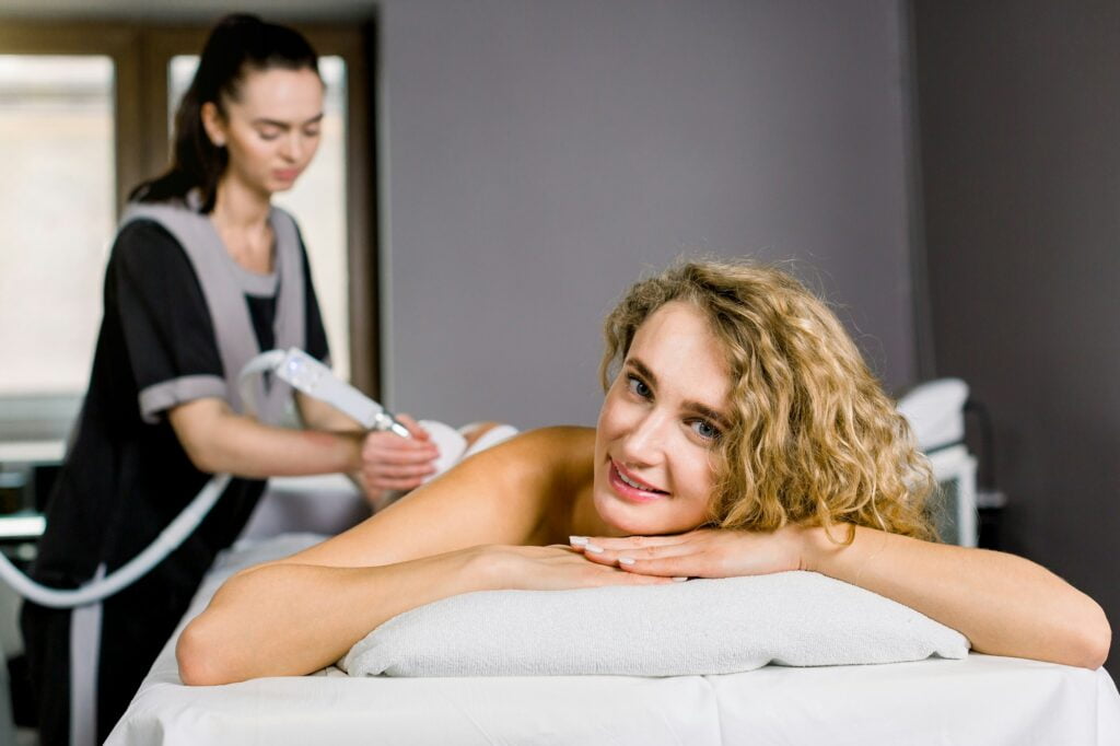 blond woman getting ultrasound cavitation treatment by cosmetologist