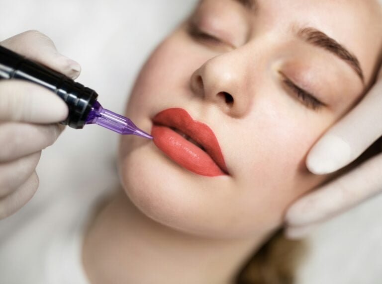 Lip Blushing Cosmetologist applying permanent make up on lips of beautiful woman